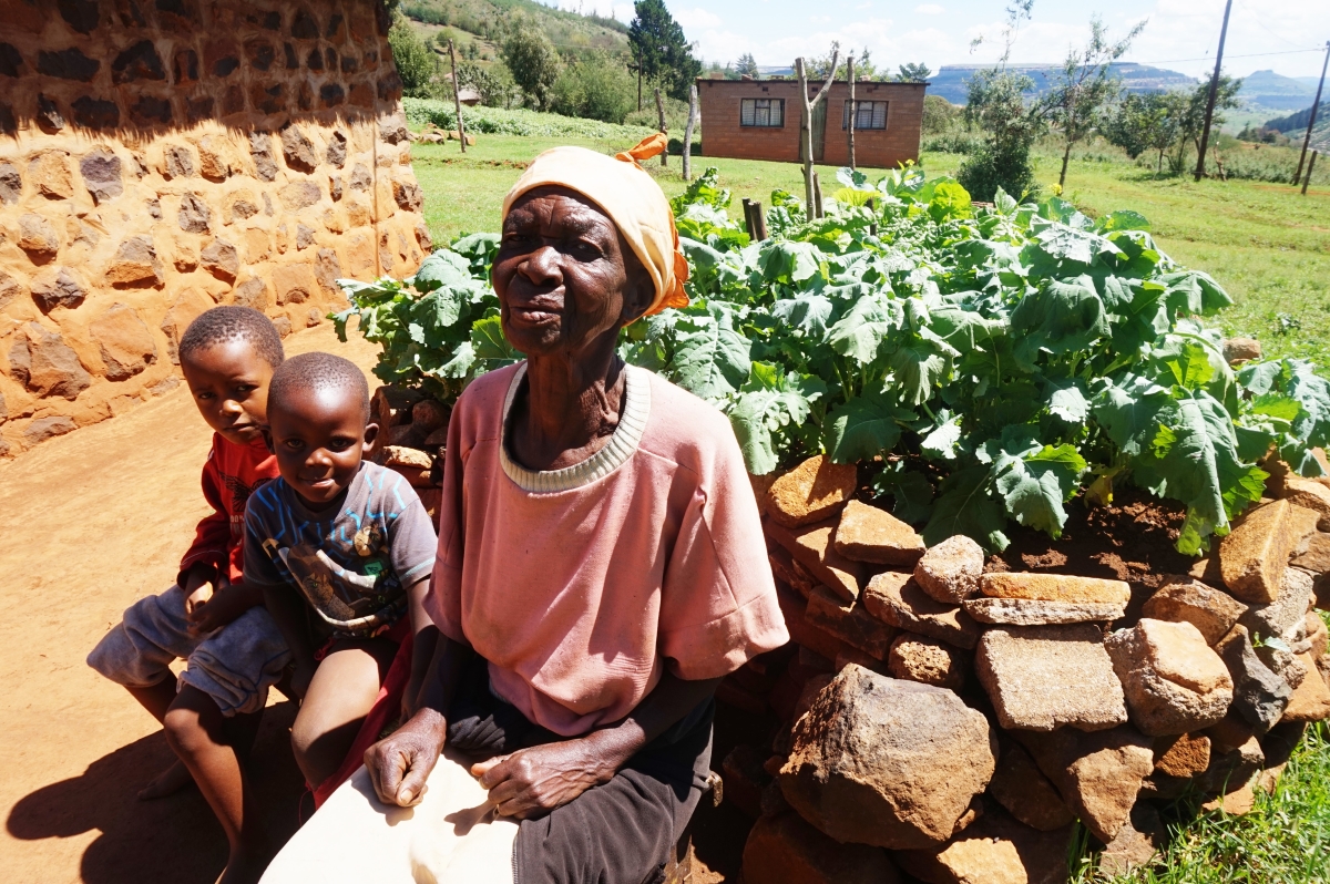 A granny sits with two young grandsons near her keyhole garden. The garden is a fresh food sourse for the family.